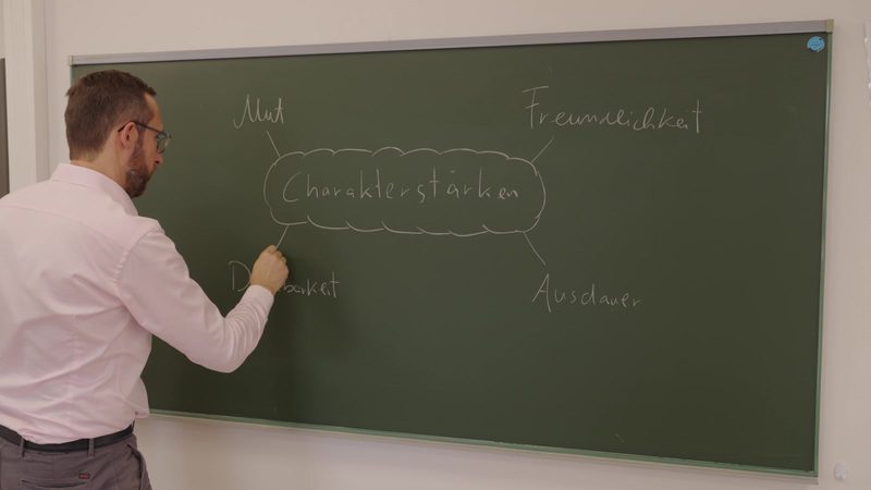 Roland Bernhard writing character strengths on a blackboard: courage, kindness, gratitude, perseverance